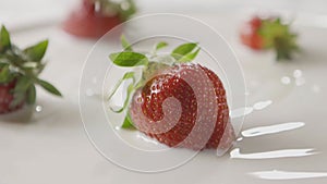 Milk splash on a ripe red strawberry fruit, which lies on a white plate with milk. Slow motion. A few berries lie on the