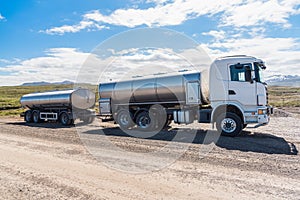 Milk tanker with a trailer stationary along a gravel road on a sunny day