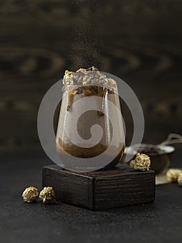 Milkshake with caramel sauce decorated by caramel popcorn and chocolate powder on green background.