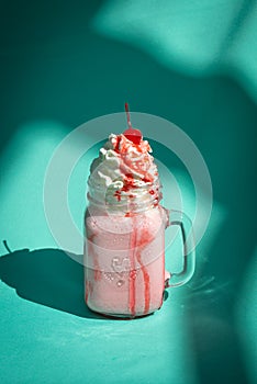 Milkshake with a cherry and whipped cream on mint turquoise background with abstract shadows.