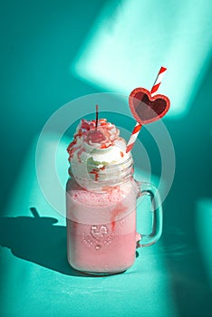 Milkshake with a cherry and whipped cream on mint turquoise background with abstract shadows.