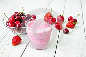 Milkshake made of mix - cherry and strawberry and tasty berries on white wooden table.
