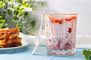 a milkshake with strawberries and topping in a glass stands on a blue tile