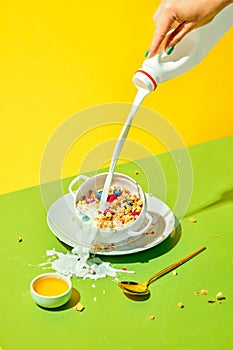 Milky breakfast. Woman pouring milk into cereal bowl, muesli with berries against green yellow background