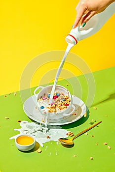 Milky breakfast. Woman pouring milk into cereal bowl, muesli with berries against green yellow background