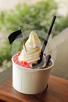 Milky ice cream soft serve in paper cup topping with chocolate ball and red jelly
