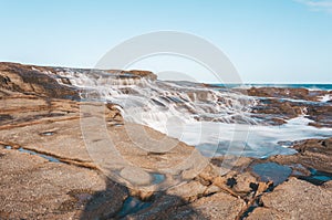 Milky ocean cascades flowing over honey coloured rocks