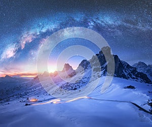 Milky Way over snowy mountains and car headlights on the road
