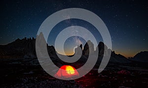 Milky way over Three Peaks of Lavaredo, with lighted camping tent on the foreground