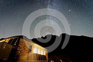 Mliečna dráha a obloha plná hviezd nad osvetlenou vysokohorskou chatou a pohorím, Slovensko, Európa