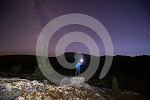 Milky way and starry sky over night scene outdoors in the forest and the mountains with girl in blue clothes and flashlight in the