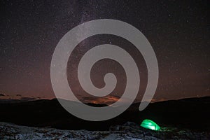 Milky way and starry sky over night scene outdoors in the forest and the mountains with green tent infront.