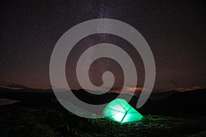 Milky way and starry sky over night scene outdoors in the forest and the mountains with green tent infront.