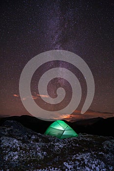 Milky way and starry sky over night scene outdoors in the forest and the mountains with green tent infront.
