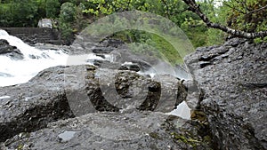 Milky white massive long waterfall down slippery valley rocks and stones in summer