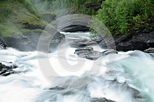 Milky white massive long waterfall down slippery valley rocks and stones in summer, long exposure