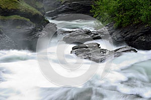 Milky white massive long waterfall down slippery valley rocks and stones in summer