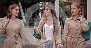 Millenial brunnette woman talking to her friends with shopping paper bags while walking at street. Happy female chatting