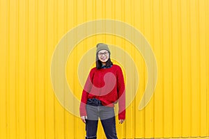 Millenial girl im fashionable clothes having a good time, making funny faces near bright yellow urban wall.
