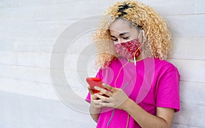 Millenial girl using mobile phone while wearing face mask during coronavirus outbreak - Female teenager having fun with new trends photo