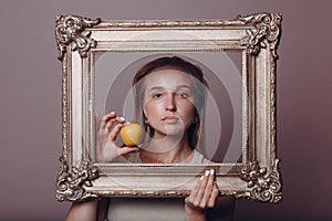 Millenial young woman blonde hair holds gilded picture frame in hands face portrait