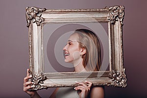 Millenial young woman blonde hair holds gilded picture frame in hands face portrait