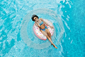 Millennial African American girl in sexy swimwear floating on donut ring at pool
