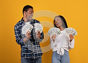 Millennial african american male and female hold many dollars in hands and expressing success