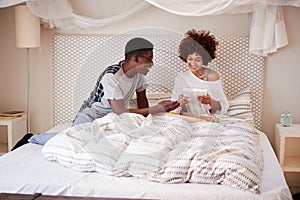 Millennial African American man giving his partner breakfast and gifts in bed to celebrate