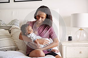 Millennial African American  mother  sitting on her bed holding her three month old baby son in her arms