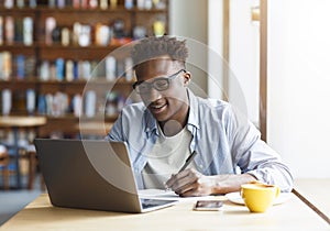 Millennial African American student with laptop taking notes in cafe