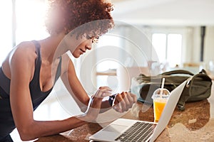 Millennial African American woman checking fitness app on watch and laptop after workout, side view