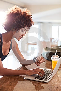 Millennial African American woman checking fitness app on watch and laptop after workout, vertical