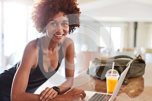 Millennial African American woman checking fitness data on laptop after gym smiling to camera