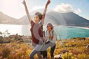 Millennial African American woman hiking by the coast with a friend celebrates reaching summit