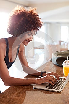 Millennial African American woman using laptop to check fitness data after her work out, vertical