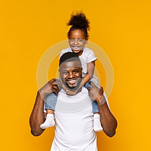 Millennial african father riding his little daughter on shoulders