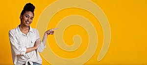 Millennial afro girl pointing aside at copy space on yellow background