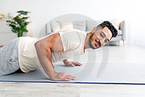 Millennial Arab man standing in plank pose on yoga mat, doing strength exercises at home