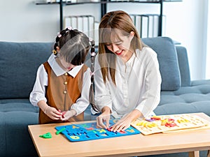 Millennial Asian happy cheerful little cute preschooler daughter girl playing learning alphabets letters jigsaw toy on living room