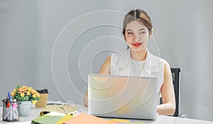 Millennial Asian happy cheerful pretty businesswoman secretary employee sitting smiling enjoy working online typing laptop