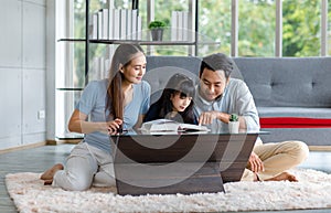 Millennial Asian happy family father and mother sitting on cozy carpet floor smiling helping teaching little young girl daughter