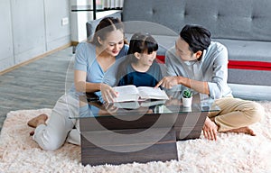 Millennial Asian happy family father and mother sitting on cozy carpet floor smiling helping teaching little young girl daughter