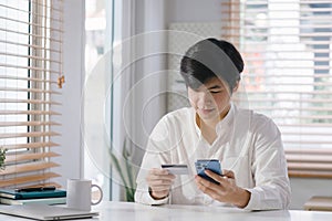 A millennial Asian man paying with credit card online while making orders via mobile Internet making transaction using