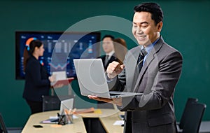 Millennial Asian professional successful male businessman in formal business suit standing holding laptop computer showing fist up