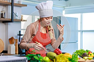 Millennial Asian young cheerful female housewife chef wearing white tall cook hat and apron standing smiling waving hand smelling