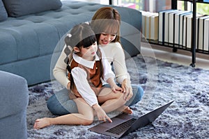 Millennial Asian young female teenager mother nanny babysitter sitting on carpet floor helping teaching homework via laptop