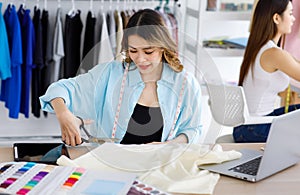 Millennial Asian young professional female designer dressmaker businesswoman with measuring tape using scissors cutting fabric