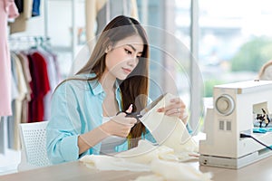 Millennial Asian young professional female designer dressmaker businesswoman with measuring tape using scissors cutting fabric