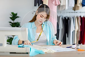 Millennial Asian young professional female designer dressmaker businesswoman with measuring tape using scissors cutting fabric photo